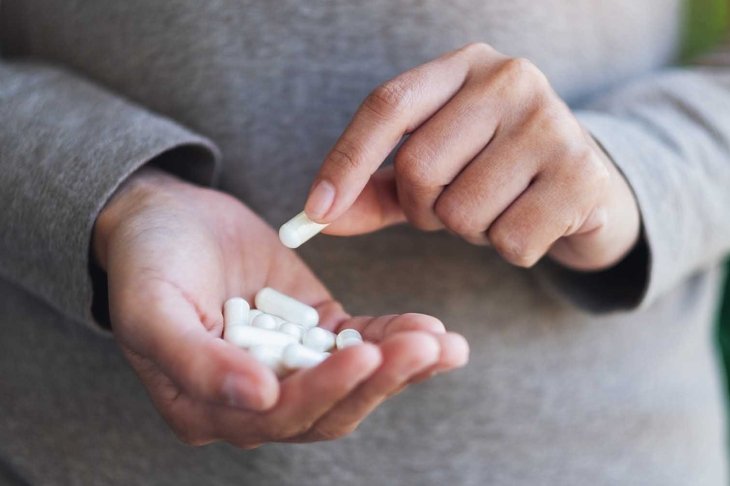 Closeup image of a woman holding and picking white medicine capsules in hand