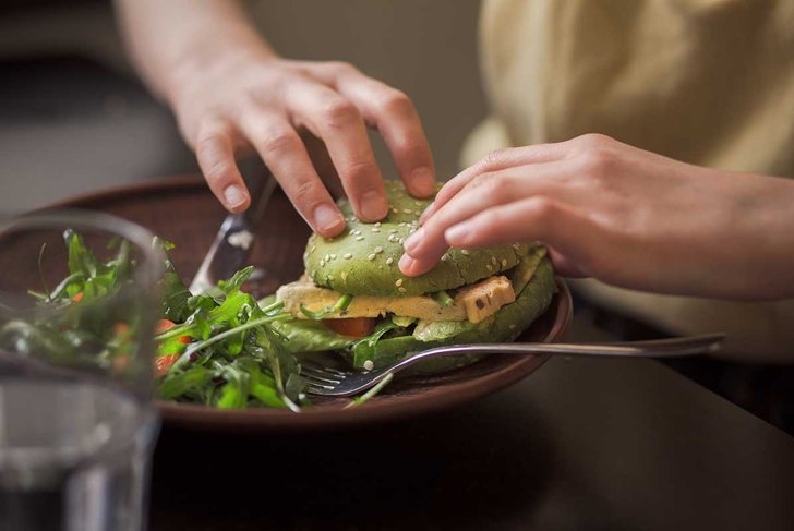 Picture of vegan dish represented on wooden plate. Lady's hands taking vegan burger from plate in vegan restaurant or cafe.