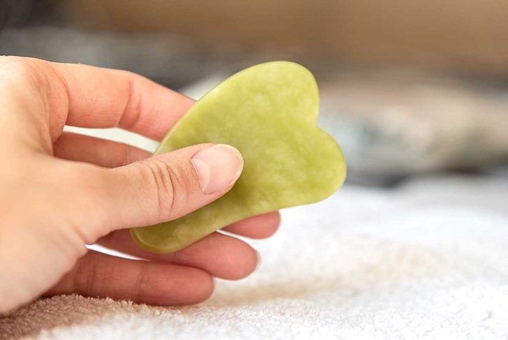 Female hand holding green gua sha facial massager